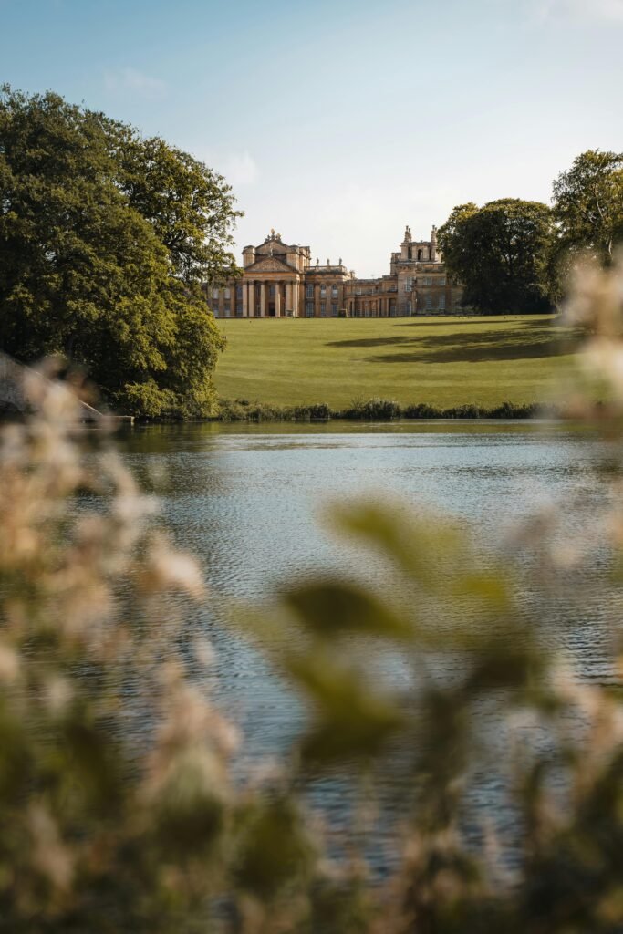A picturesque view of Blenheim Palace in Woodstock, England, framed by trees and water.